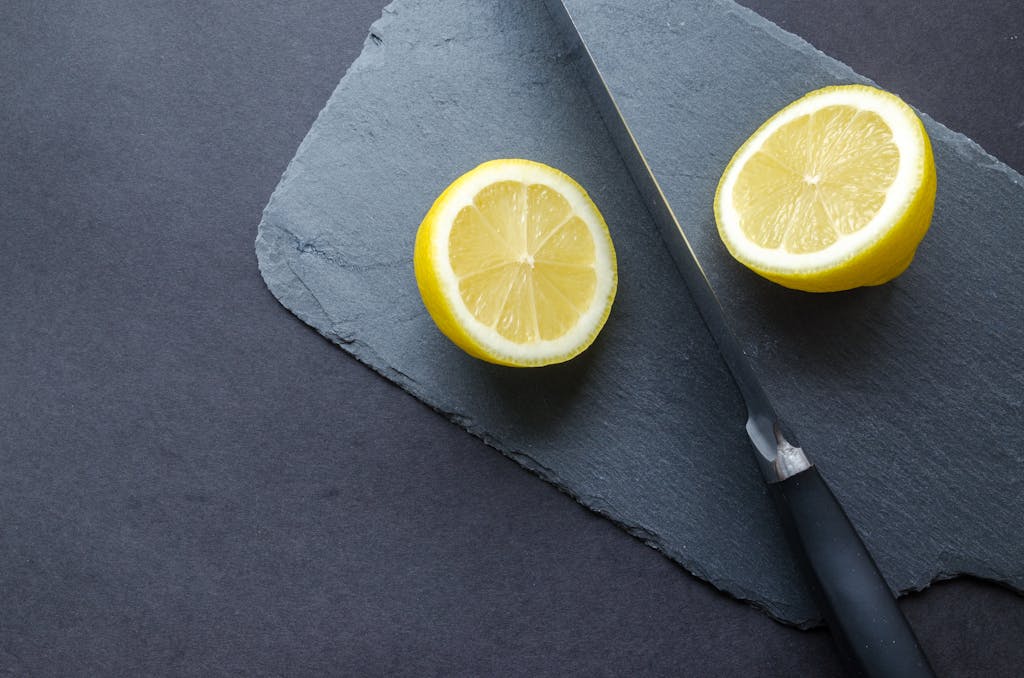 Close-up of lemon halves with knife on slate board, highlighting freshness and vibrant colors.