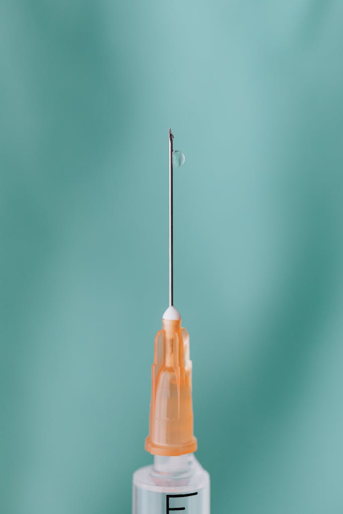 Detailed view of a syringe needle with a liquid drop, symbolizing medical care.