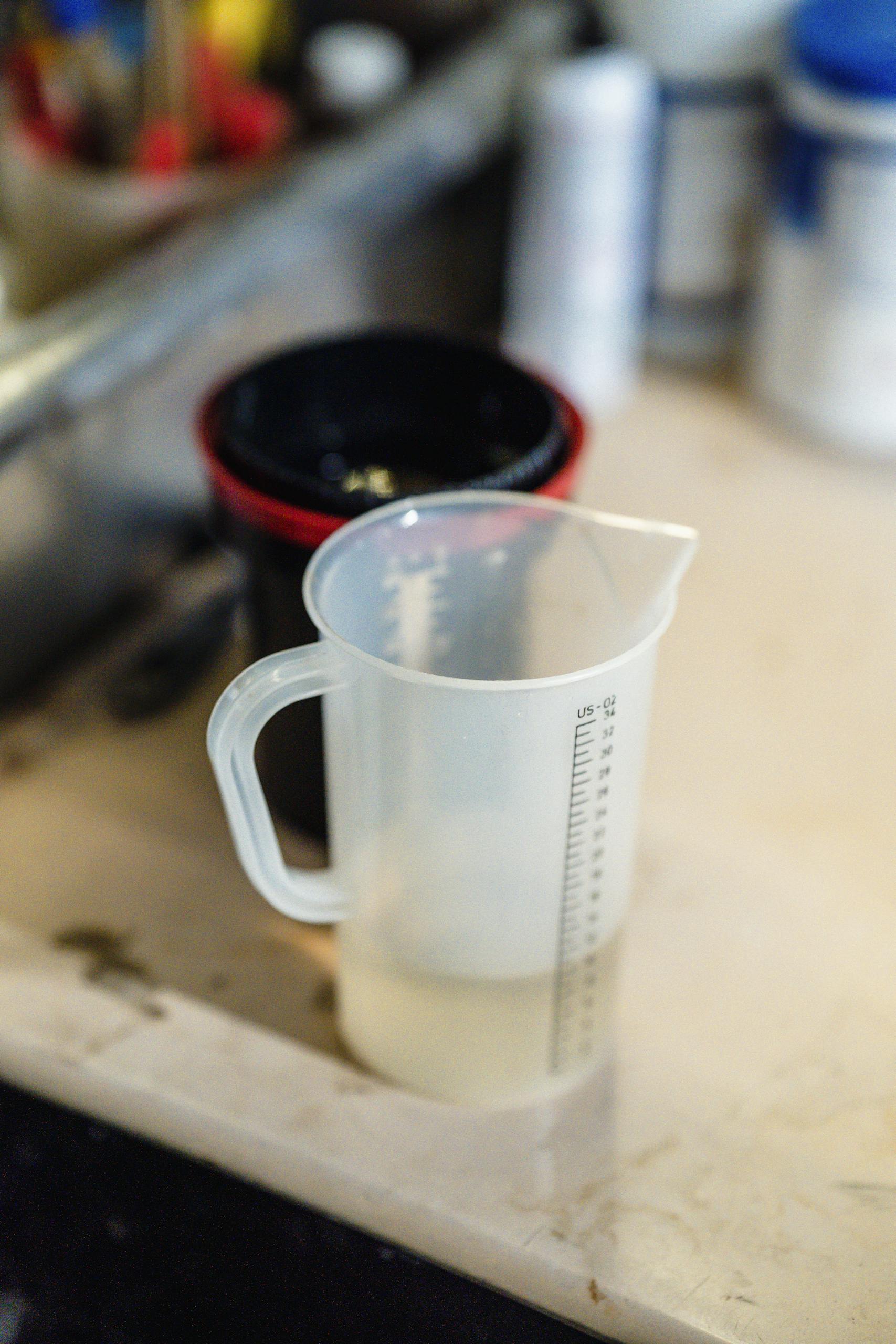 Plastic measuring cup with liquid on a kitchen table foreground.