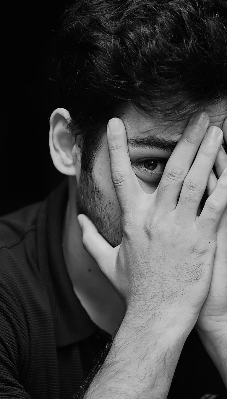 Close-up black and white portrait of a thoughtful man partially covering his face with hands.