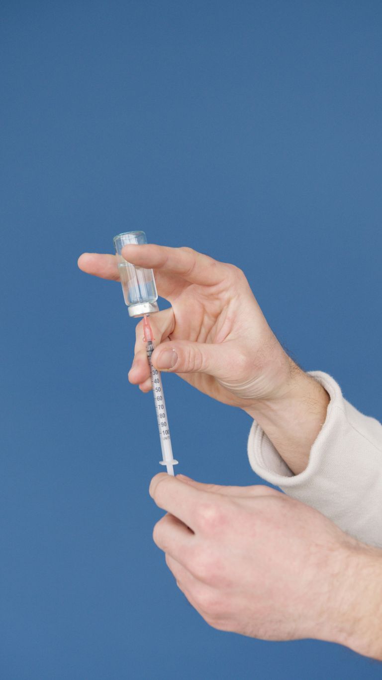 Close-up of hands filling a syringe with a vaccine from a vial against a blue background.